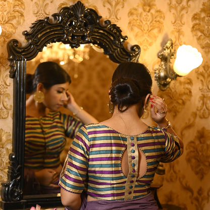 Detail shot of golden silk fabric with purple and green stripes and decorative buttons on sleeves.