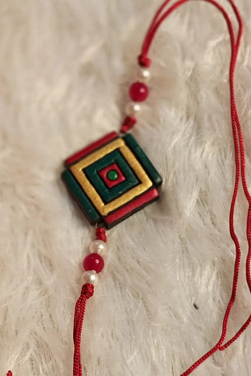 Green and gold geometric terracotta rakhi with pearls and red beads – handmade Bengal clay Raksha Bandhan thread by Bong Trendz
