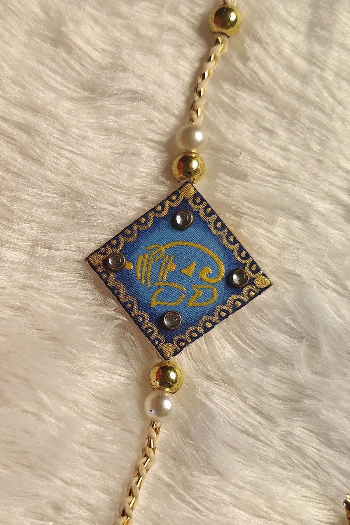 Hand-painted Ganesha fabric rakhi in royal blue with pearls – auspicious Raksha Bandhan thread by Bong Trendz