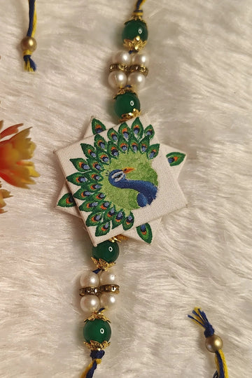 Hand-painted peacock fabric rakhi with green beads and pearls – Bengal-art Raksha Bandhan thread by Bong Trendz