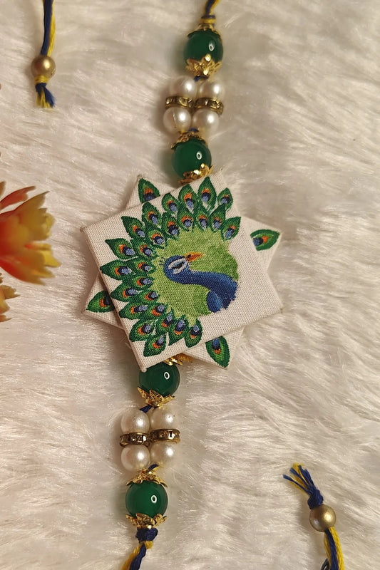 Hand-painted peacock fabric rakhi with green beads and pearls – Bengal-art Raksha Bandhan thread by Bong Trendz