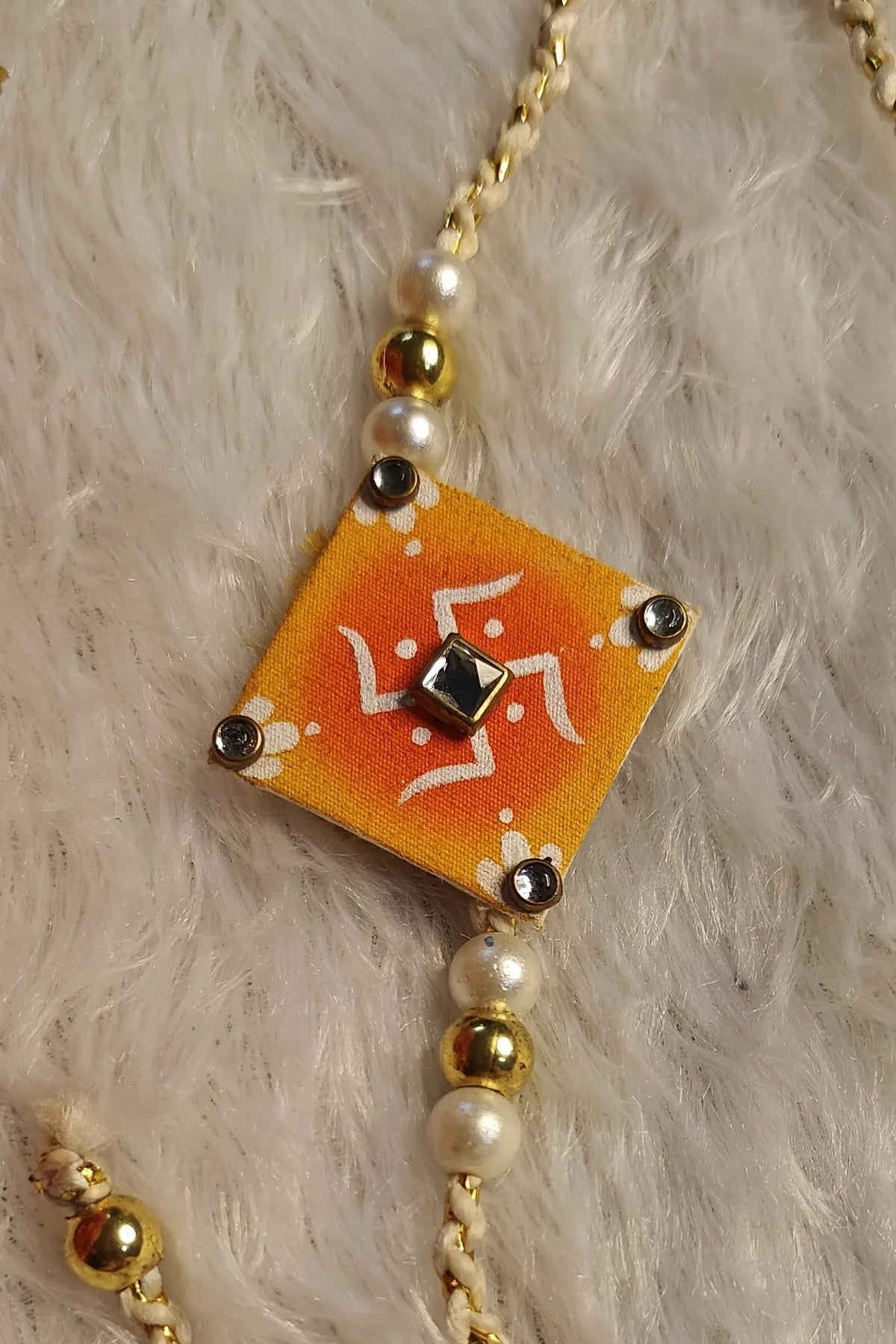 Hand-painted alpona fabric rakhi in orange with kundan and pearls – Bengal folk-art Raksha Bandhan thread by Bong Trendz