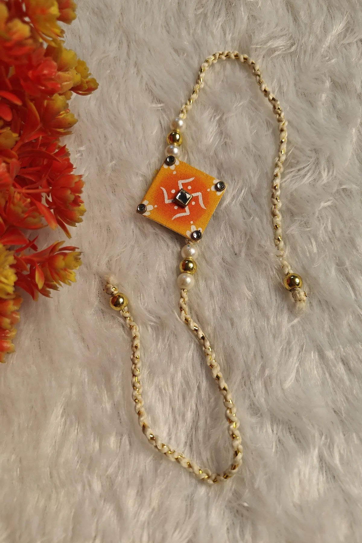 Close-up of white alpona motifs and kundan centre on an orange fabric rakhi