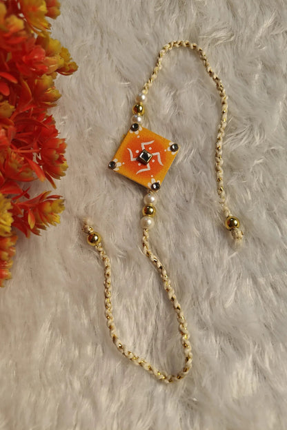 Close-up of white alpona motifs and kundan centre on an orange fabric rakhi
