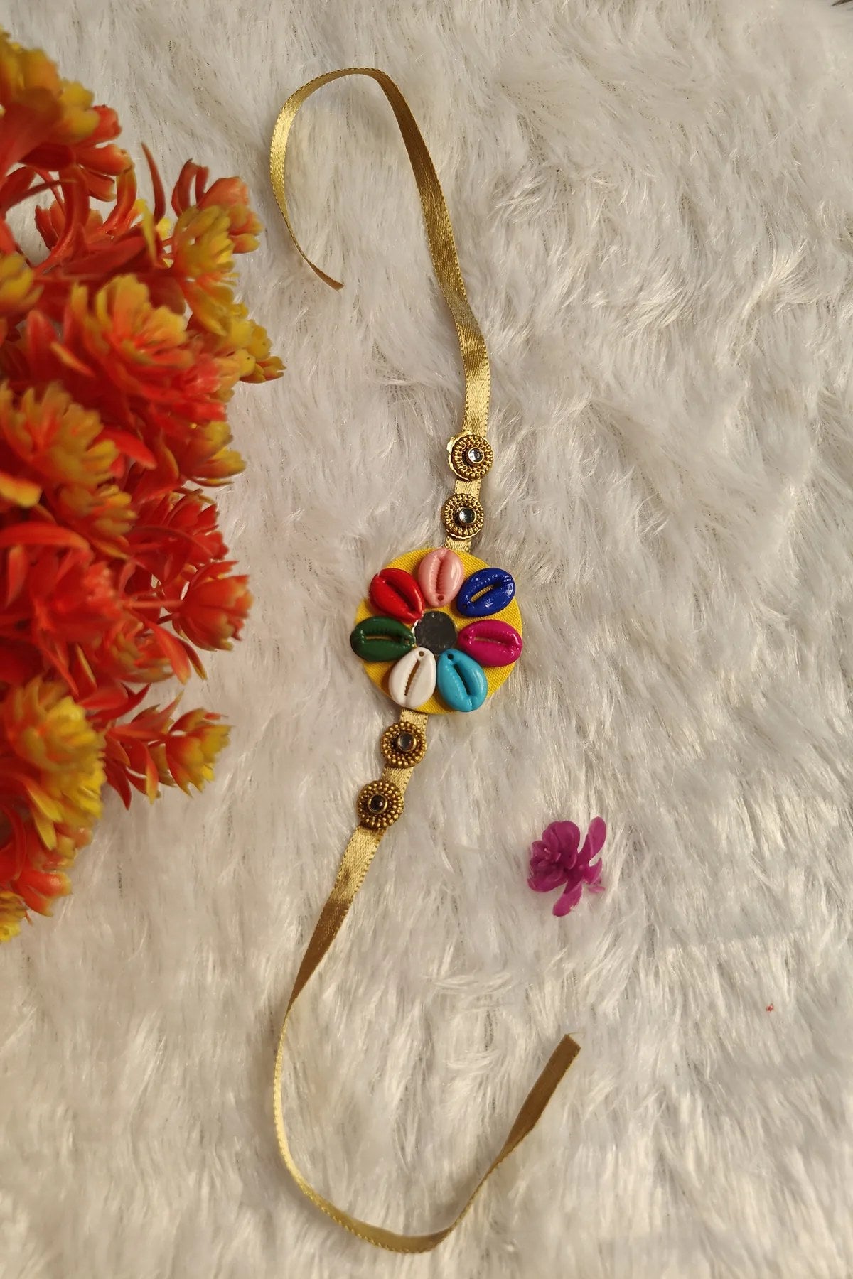 Close-up of multicolour cowrie shells on a yellow fabric disc rakhi