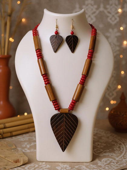 Dark carved wooden leaf pendant on bamboo tube necklace with red beads and matching leaf earrings displayed on a white jewellery bust