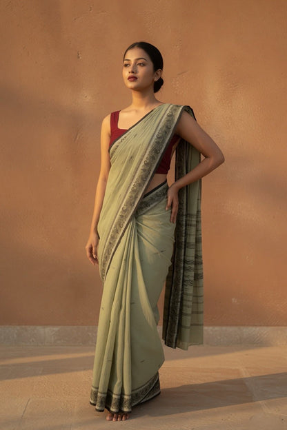Konika olive green Shantipur handloom cotton saree, model looking away, maroon blouse and dark floral border