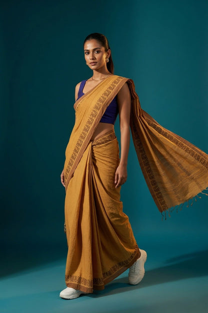 Patrangi mustard Shantipur handloom check cotton saree walking pose with brown leaf-motif border