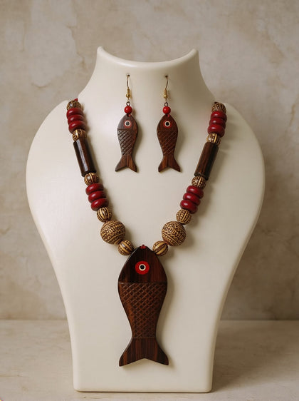 Hand-carved wooden fish pendant necklace with red and carved beige beads and matching fish earrings displayed on a white bust
